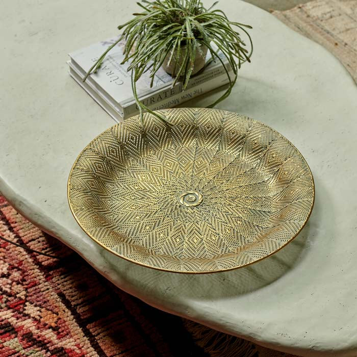 Large round gold tray sat on an off white coffee table with a plant