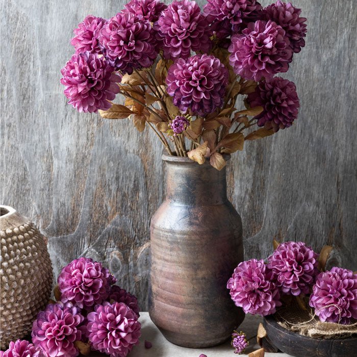 Styled image of a bouquet of bright pink fake flowers arranged in a brown stoneware vase.