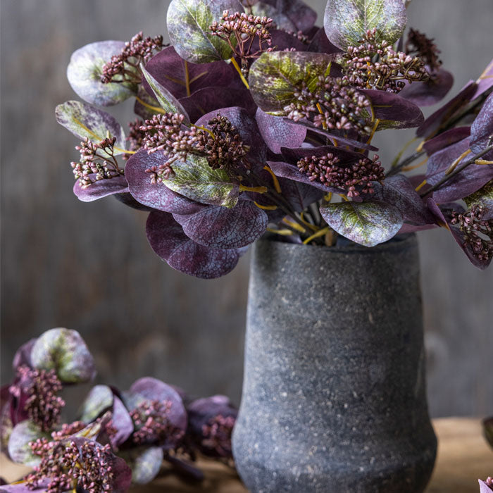 Artificial eucalyptus foliage in purple tones, displayed in brown vase.
