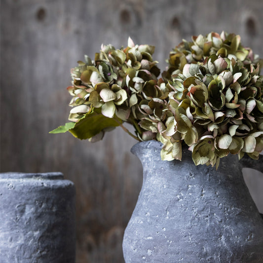Grey stone jug with artificial hydrangea flowers in faded green colour. An easy way to add a natural vibe to your home.