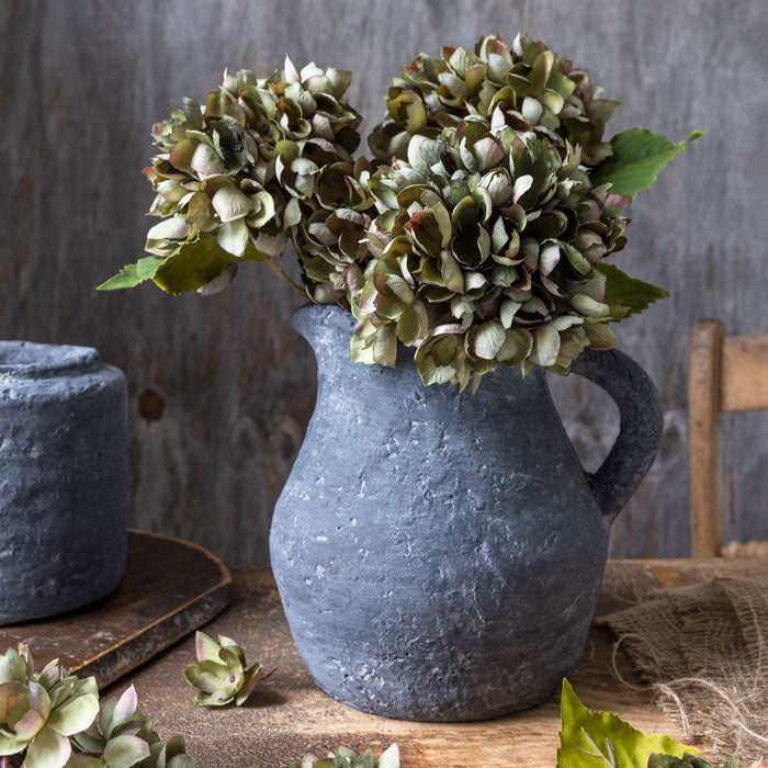 Artificial green hydrangea flowers in grey stoneware jug vase.