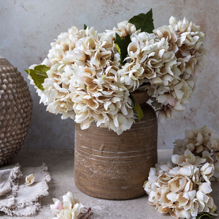 Brown ceramic vase filled with artificial cream coloured hydrangea flowers.