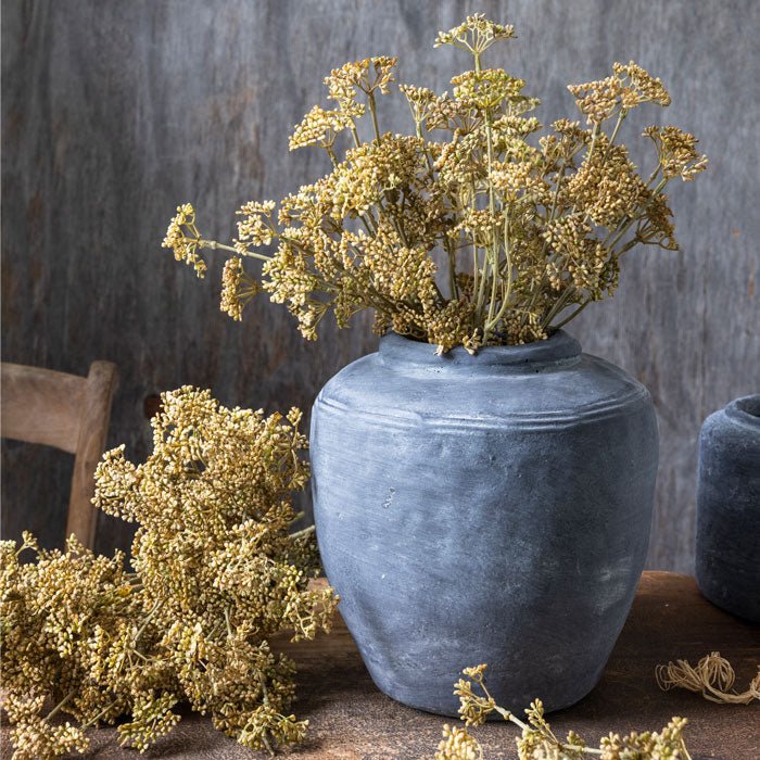 Artificial meadow flower foliage in warm yellow colour, displayed in grey stoneware vase.