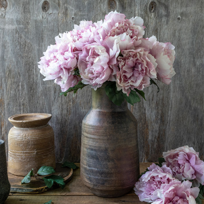 Brown ceramic vase filled with artificial pink peony flowers.
