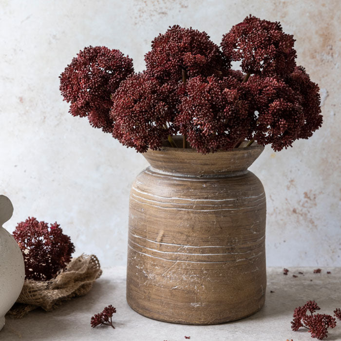 Brown ceramic vase filled with artificial sedum foliage in crimson colour.