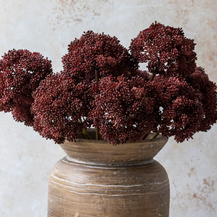 Artificial foliage crimson sedum heads in brown wood effect vase.