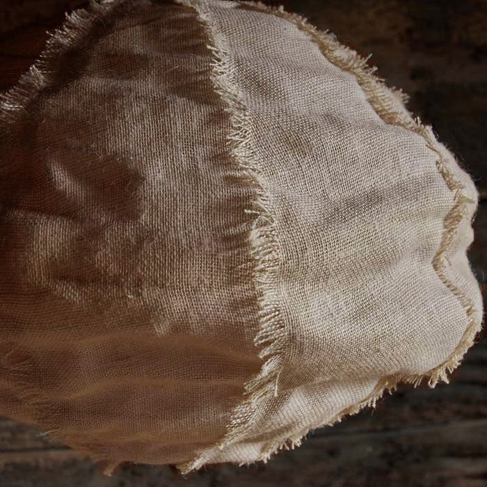 A close up of a pendant light made from fabric in a neutral colour-way with textured seams. 