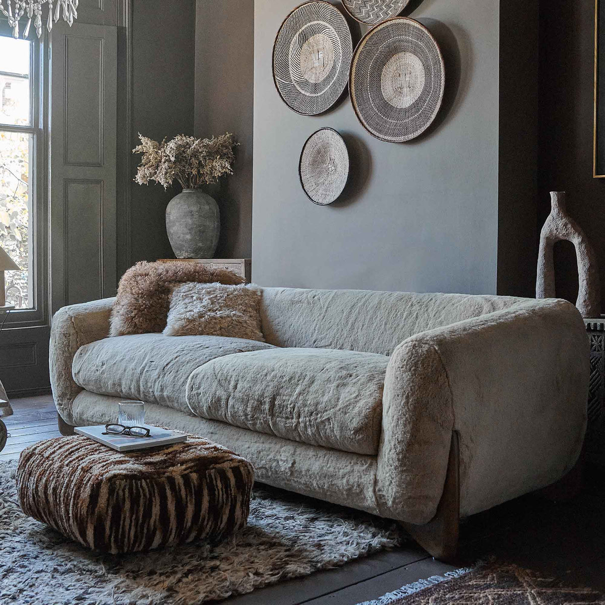 Cream faux sheepskin sofa with a soft tactile texture, rounded mid-century inspired silhouette and warm oak wooden legs. Moritz Faux Sheepskin Sofa by Abigail Ahern, designed with a generous three seater shape and deep comfortable cushioning for relaxed everyday lounging. A luxury statement sofa perfect for modern living rooms and contemporary interiors, adding cosy texture, timeless style and a sophisticated focal point to your home decor.