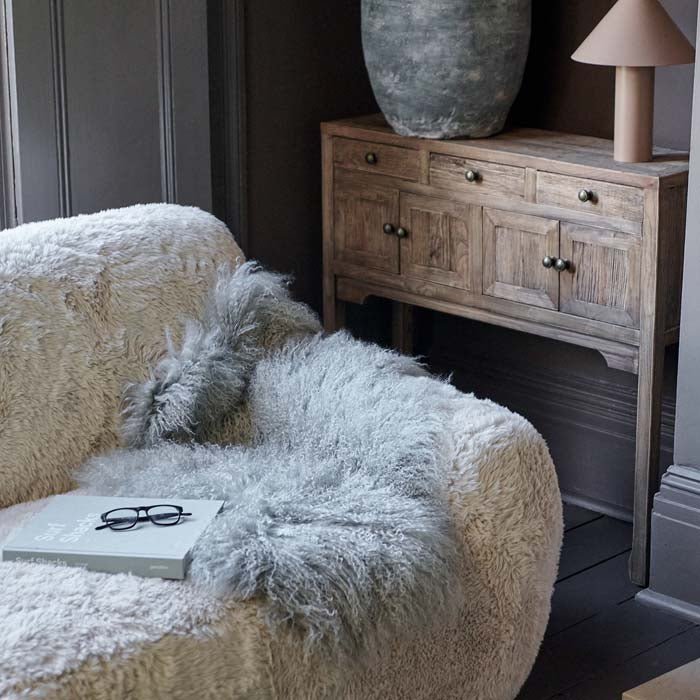 Styled image of a pale grey sheepskin draped on a cream faux fur couch