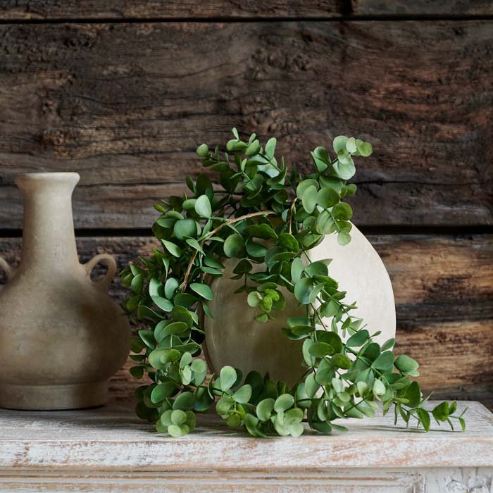 The faux trailing green eucalyptus styled in a draping way out of a ceramic vase.