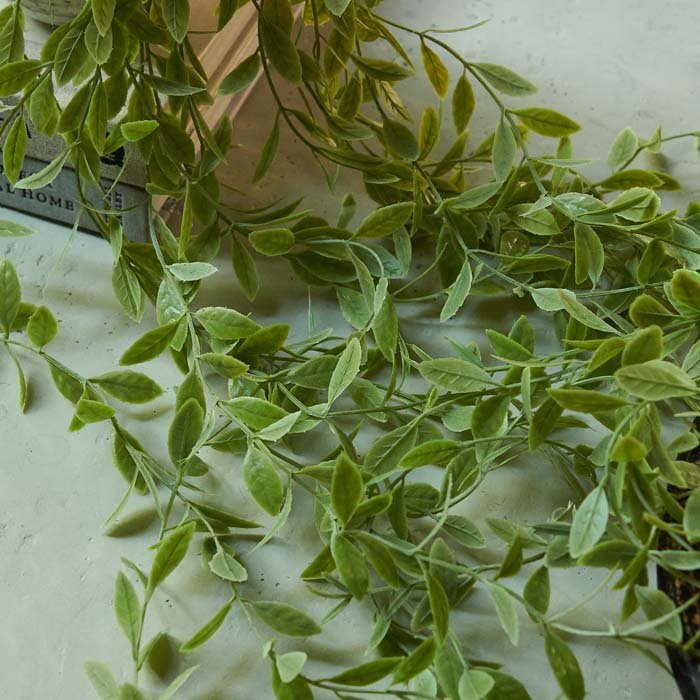 Trailing stems of artificial weeping willow on a table, covered in a lot of faux green leaves.