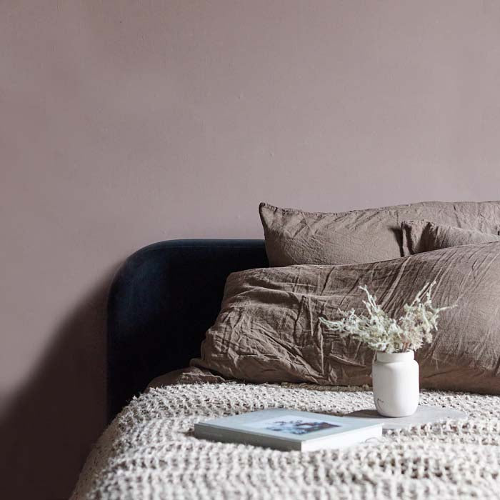 Pecan paint is a soft colour with pink undertones perfect for creating an accent wall. A bedroom wall has been styled behind a bed with soft linen pillows and a kintted throw. 