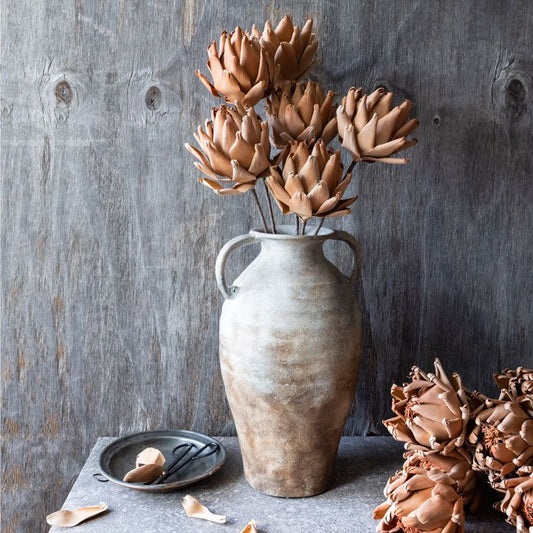 A large oversized concrete vase filled with tall artificial flowers in a shade of terracotta. Luxury artificial flowers made from stiffened paper.