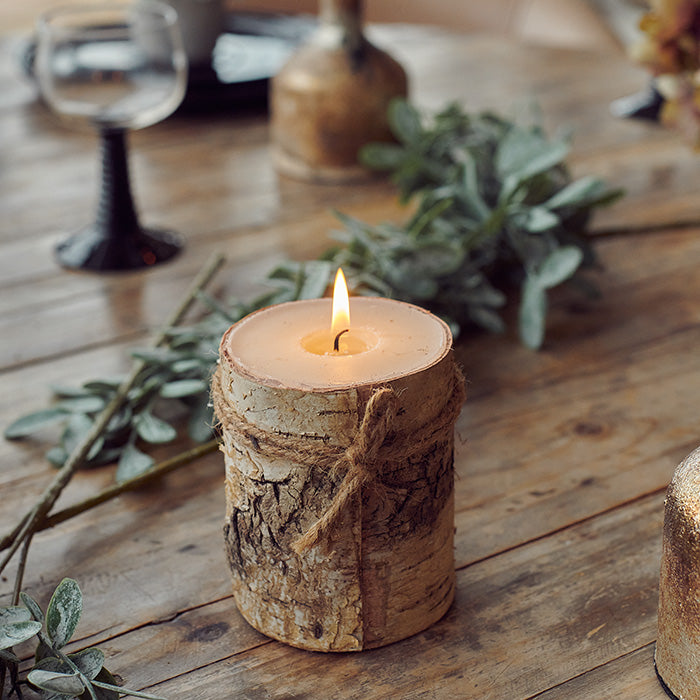 A wood log style candle wrapped with twining and set on a table top. 