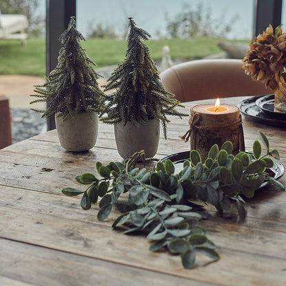 Two mini life-like pine trees laid on a festive table spread.