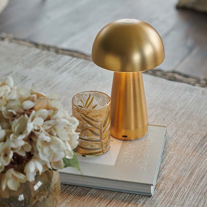 A gold metal curvaceaous mushroom shaped wireless lamp by Abigail Ahern, known for her rule breaking designs and stylish interiors. Styled on a coffee table with some books and some faux flowers, this small but mighty curvy lamp is super flexible and dimmable too, pop all over the house, style next to your bath, bedside or create intrigue to your tablescapes and a dash of metallic reflection to your kitchen worktops.