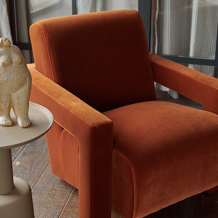 Close-up of the Abigail Ahern Phoenix Velvet Armchair in burnt orange, highlighting the rich velvet upholstery, soft tactile texture and angular detailing of the contemporary armrests.