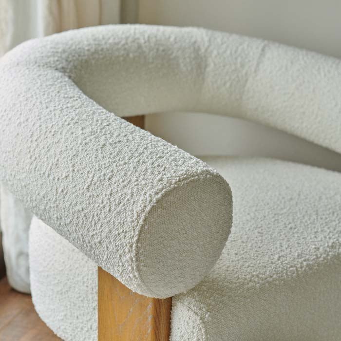 Close-up of the Abigail Ahern Ryton Cream Boucle Armchair highlighting the soft cream textured boucle upholstery and distinctive cylindrical cushion forming the curved arm and backrest.
