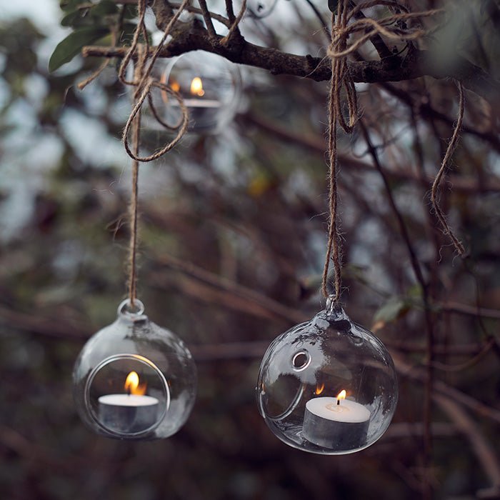 Round glass bauble tea light holders with lit tea lights hanging from a branch by twine