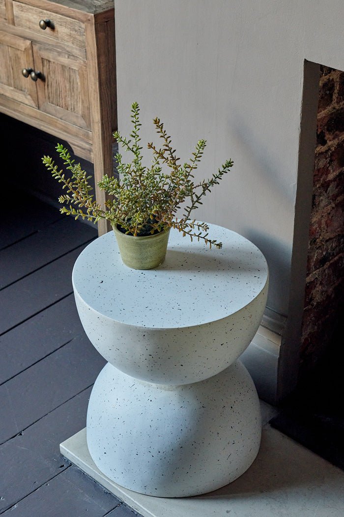 Styled image of a sculptural, speckled white side table with a small faux plant sitting on top.