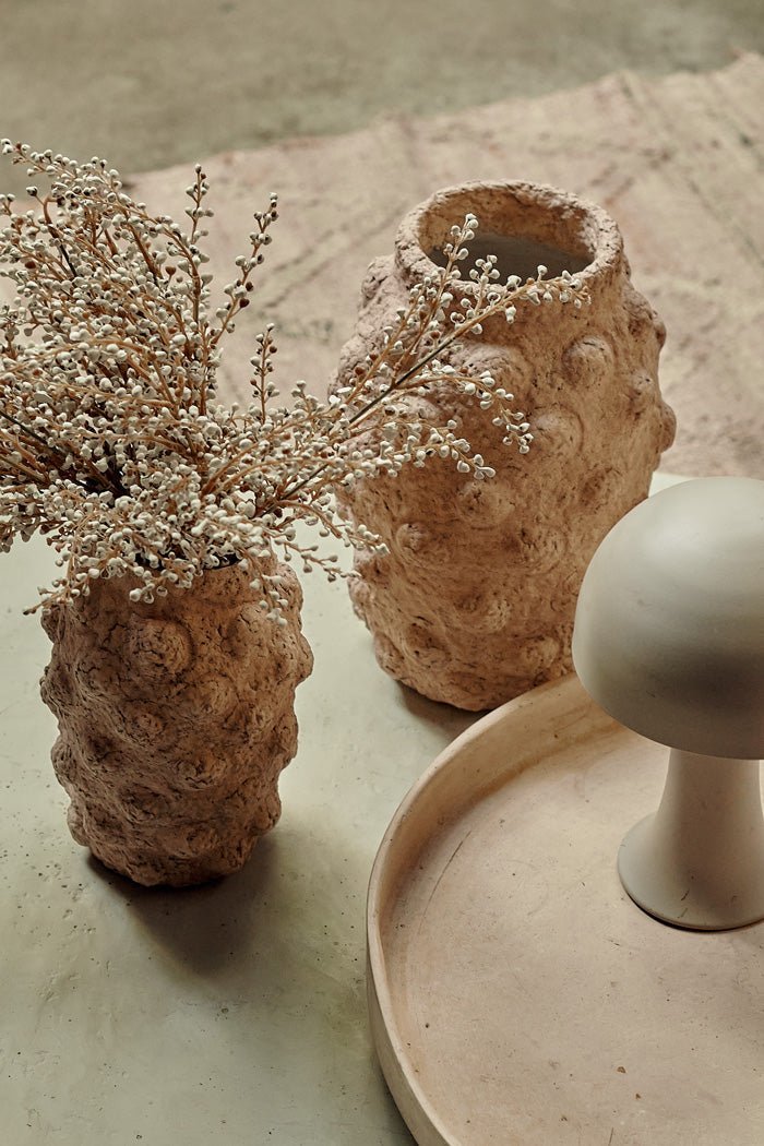 Two textured beige cement vases with a bobble texture holding some artificial cream bud stems.