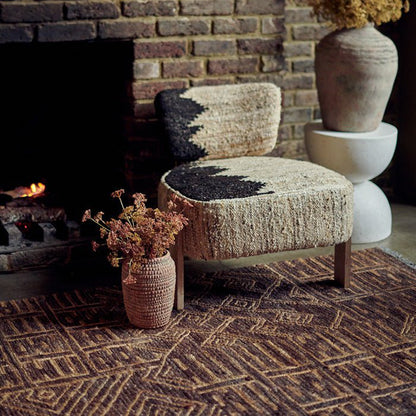 A boho accent chair sitting on a woven jute rug with a vase of artificial flowers next to it.