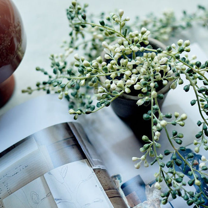 A small green faux plant in a pot with trailing buds.