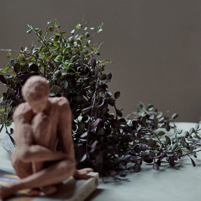 An artificial trailing dischidia plant on a table next to a small female sculpture.