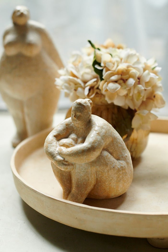 Female sculpture in a sitting position. Made from cream ceramic, she is styled with another standing sculpture to create an interesting vignette.
