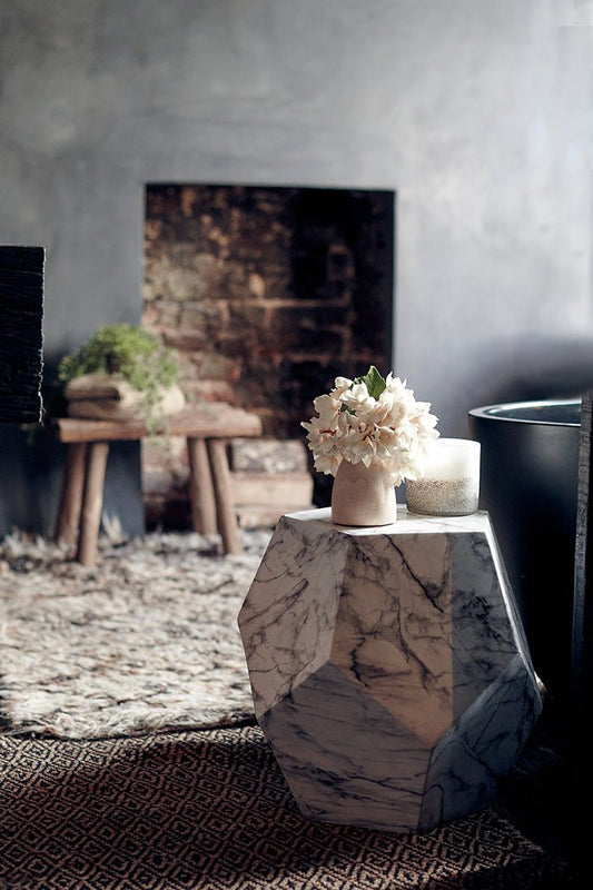 Styled image of a small, white marble side table with a vase of artificial flowers on it.