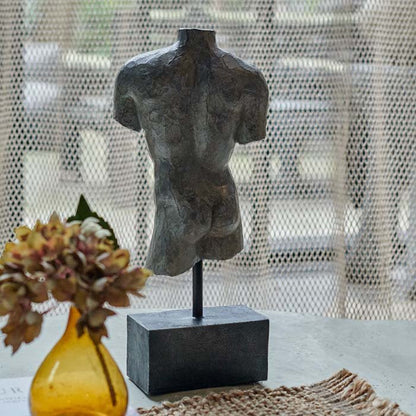Image of the back of the Adonis sculpture with a metal-like finish. Styled next to a small yellow glass vase with an artificial flower stem.