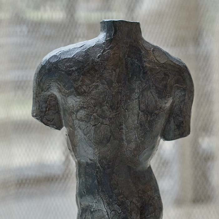 Detail image of the texture of the metal looking sculpture of a man's torso. 