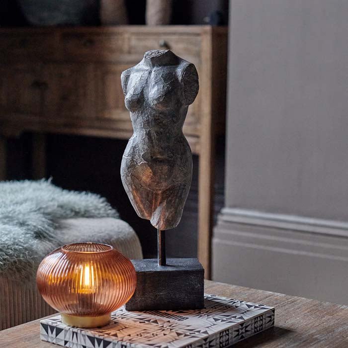 Aphrodite Scultpure, a polyresin model of a female torso with a faux metal finish mounted on a small plinth, next to a lamp. 