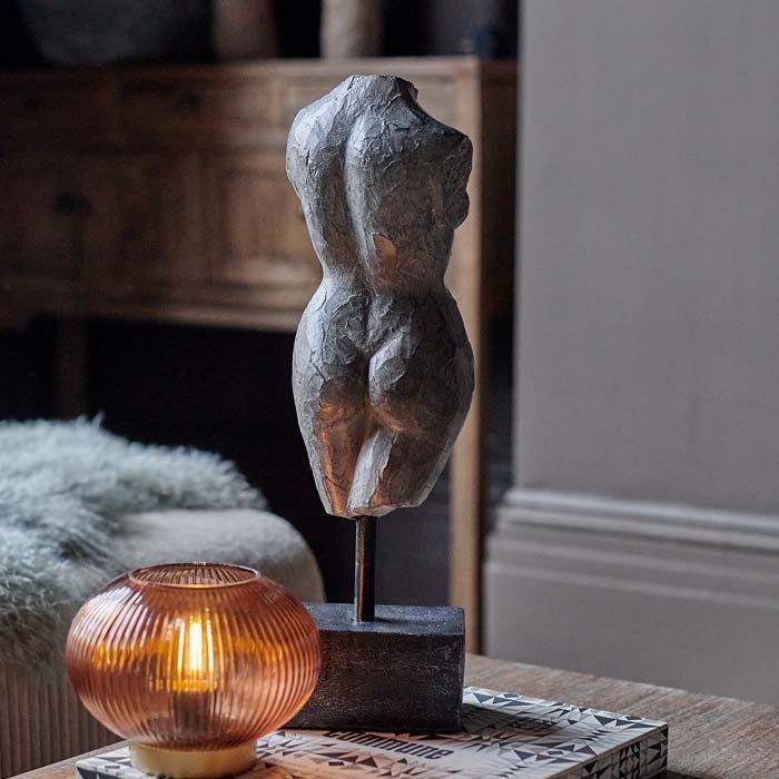 Aphrodite Scultpure, a polyresin model of a female torso with a faux metal finish mounted on a small plinth, next to a lamp. 