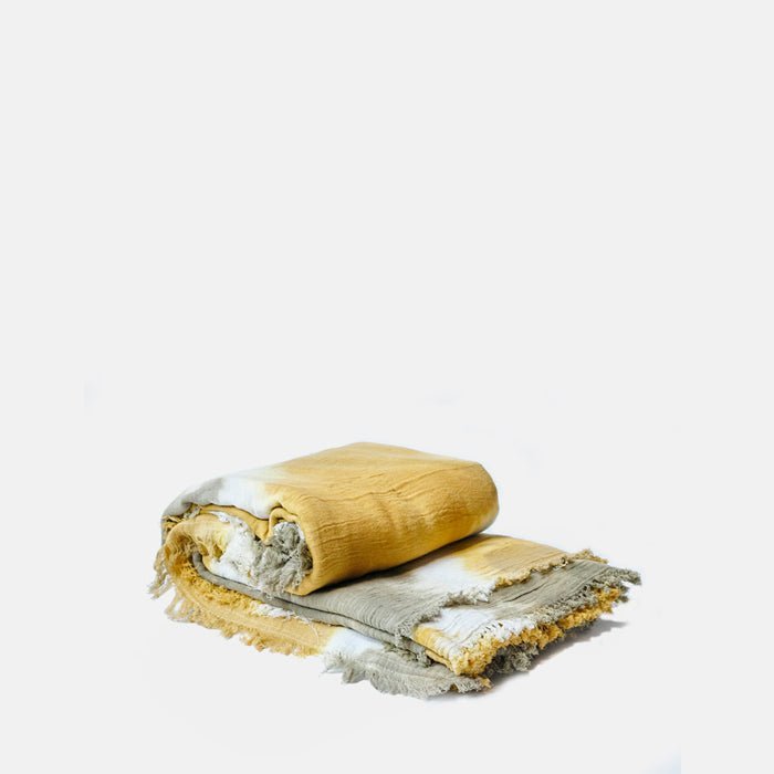 A cutout of the Saffron Bedspread, a light cotton throw in khaki and vibrant yellow with a tie-dye effect.
