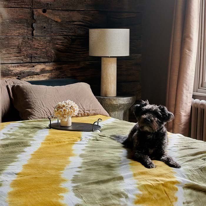 Saffron Bedspread, a light cotton throw in khaki and vibrant yellow with a tie-dye effect, on a bed with a dog perched on top