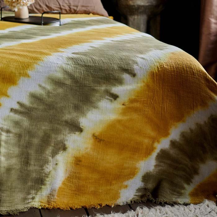 A closeup of the khaki and vibrant yellow tie-dye effect cotton fabric of the Saffron Bedspread.