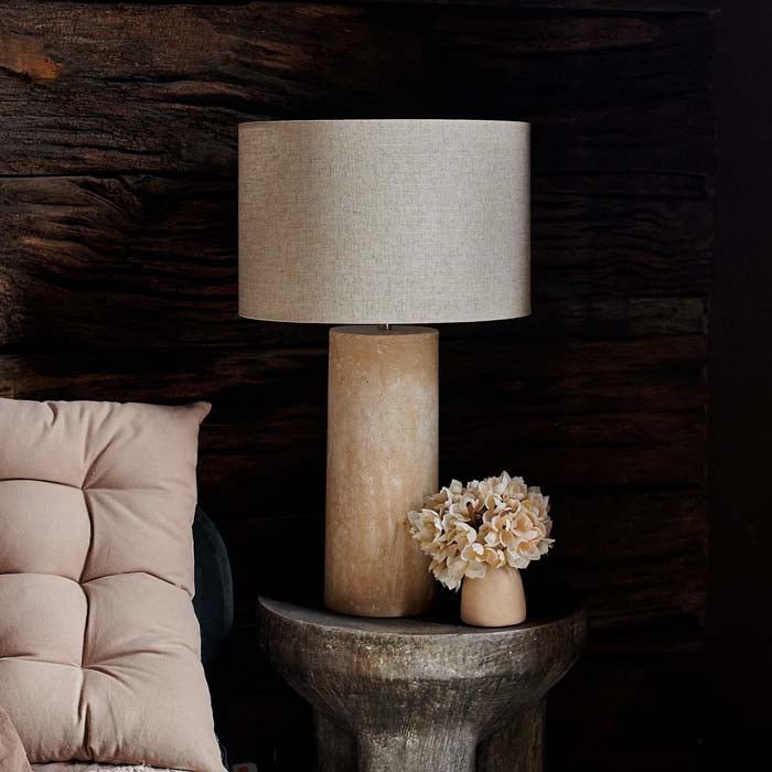 The Sennen Table Lamp on a small bedside table, next to a padded headboard cushion.