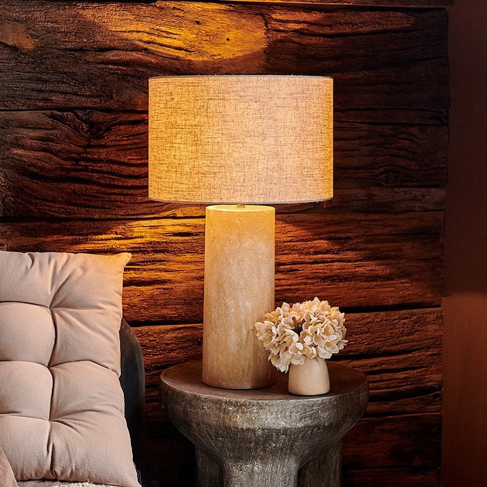The Sennen Table Lamp, warmly lit next to a padded headboard cushion.