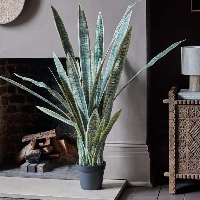 The Artificial Snake Plant in Pot, a tall faux plant with long light green pointed leaves in a small dark grey pot.