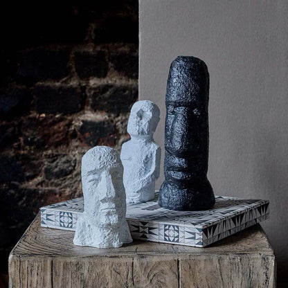 Vignette of three figurative and face sculptures on a wooden side table. Two of them are white sculptures ornaments, and one is a black sculpture.
