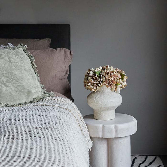 Willow is a luxury paint colour for walls, ceilings and interior woodwork. The lovely soft brown colour has been styled behind a bed with natural linen pillows, a side table with a vase of faux hydrangeas.