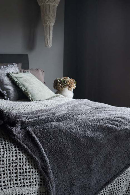A soft grey blanket styled on a double bed. Adds a cosy feel to your bedroom or extra layers for your sofa. Shop now from Abigail Ahern, rated excellent on Trustpilot.