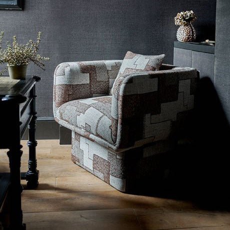 A patterned armchair with a modern design, featuring earthy brown and cream hues, positioned in a room with dark walls and wooden flooring.