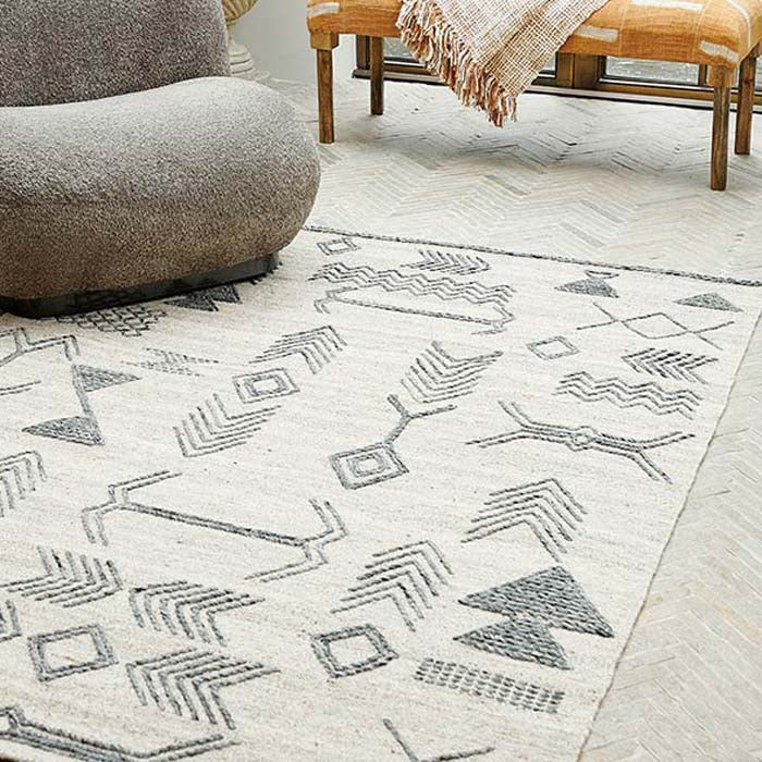 The Tampa Wool Rug, a cream rug with a beautiful black pattern in aztec style designs with a grey boucle chair.