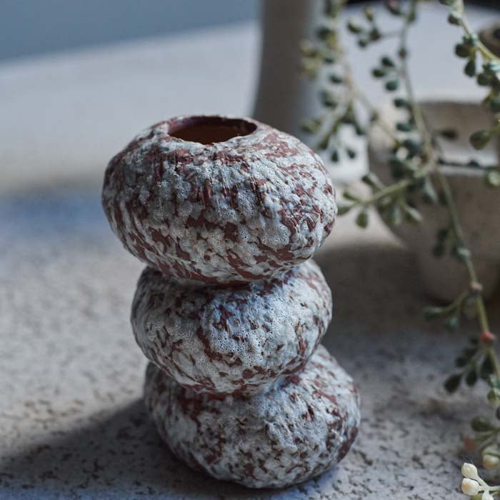 Close up image of an organically curved small brown vase with a speckled white pattern. The vase has a handmade look.