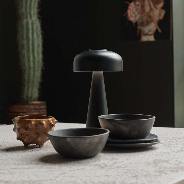 A modern rechargeable table lamp in a black finish next to some bowls.