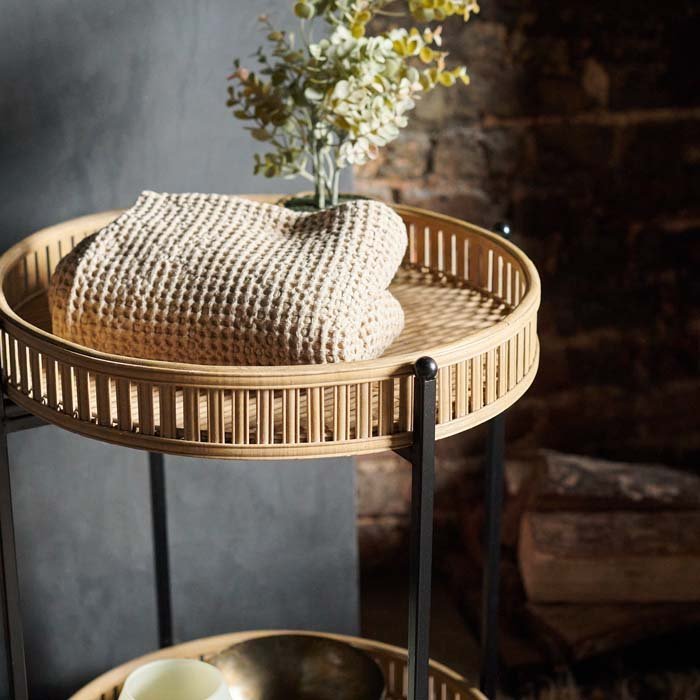 A side view of the Casoni Bamboo Side Table, styled with a folded towel and a small potted plant.
