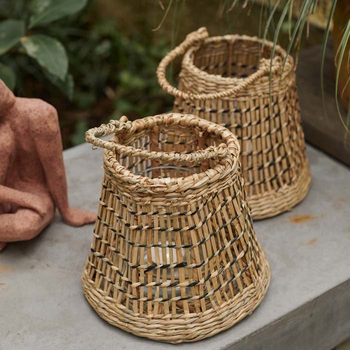 Etelle Seagrass Lantern, a small drum-shaped woven seagrass lantern with a handle, sits on a table with a matching lantern.