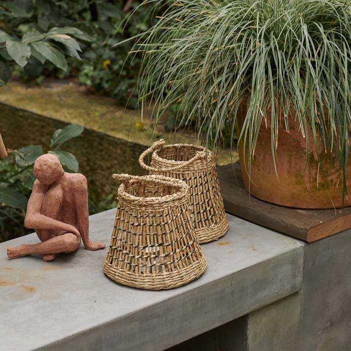 Etelle Seagrass Lantern, a small drum-shaped woven seagrass lantern with a handle, sits on a table with a matching lantern.